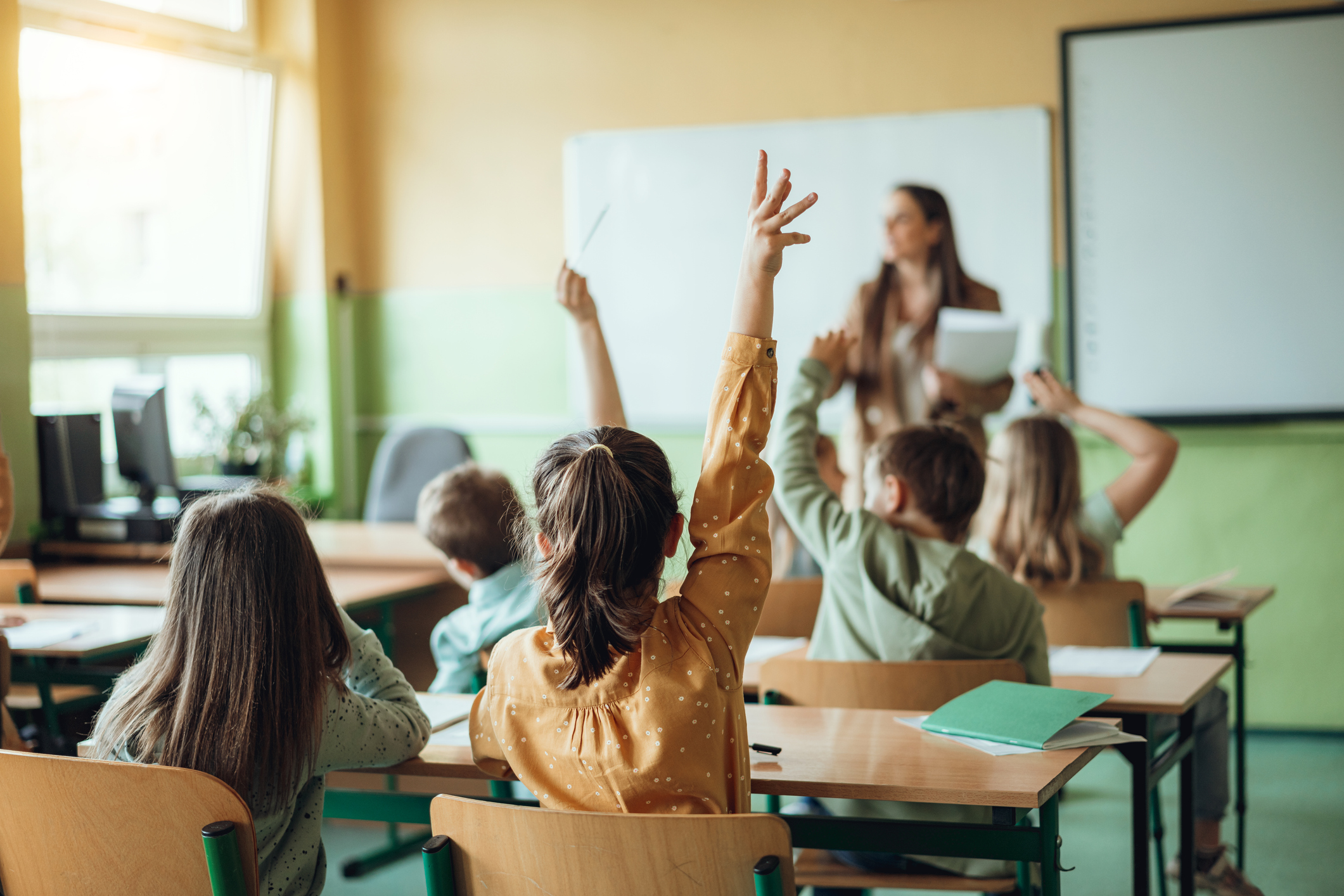 Students raising hands while teacher asking them questions in classroom